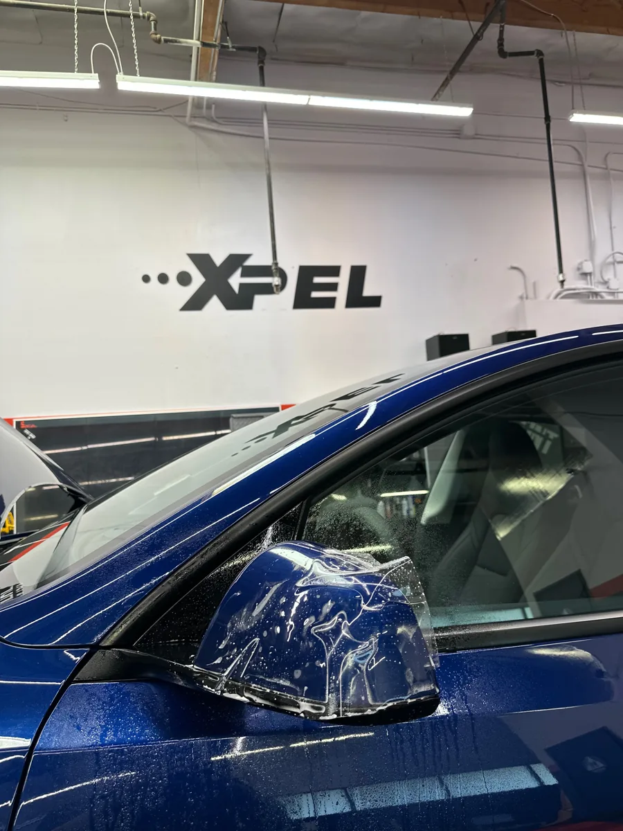 Protective film being fitted around a blue vehicle mirror